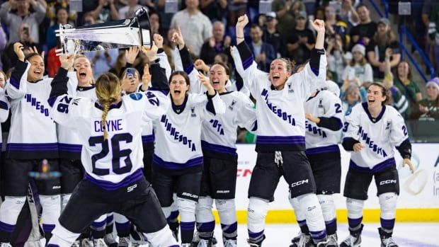 PWHL hockey players wearing Minnesota jersey celebrate with a championship trophy.