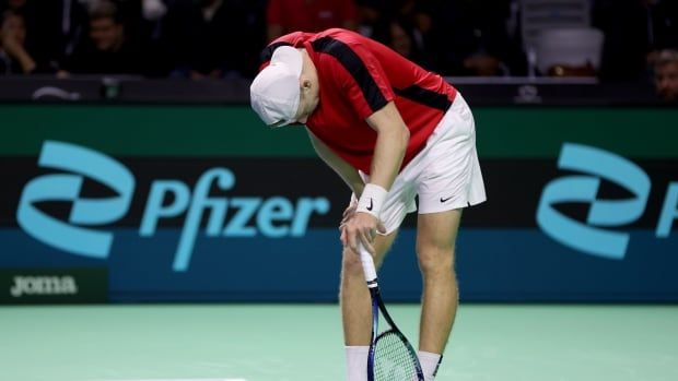 A men's tennis player leans on his racket, hanging his head, during a match.