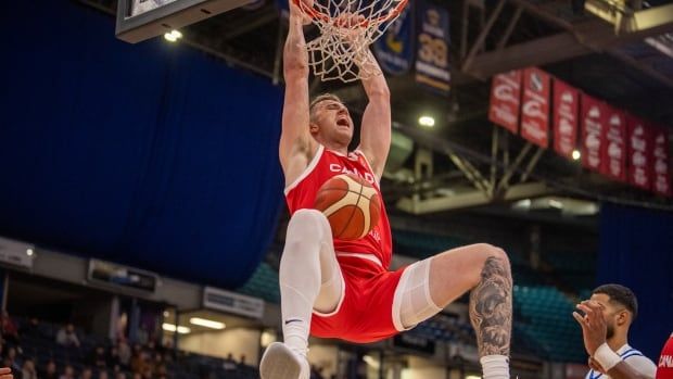 A men's basketball player hangs from the rim and shouts after dunking the basketball.