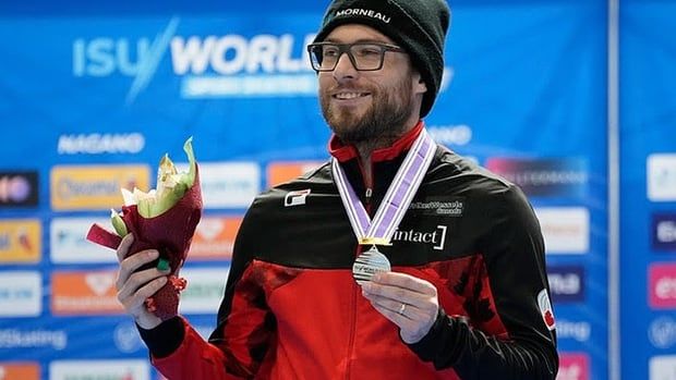 Canadian men's speed skating Laurent Debreuil holds his silver medal with his left hand  while standing at the podium at the World Cup season opener in Nagano, Japan on Nov. 22, 2024.