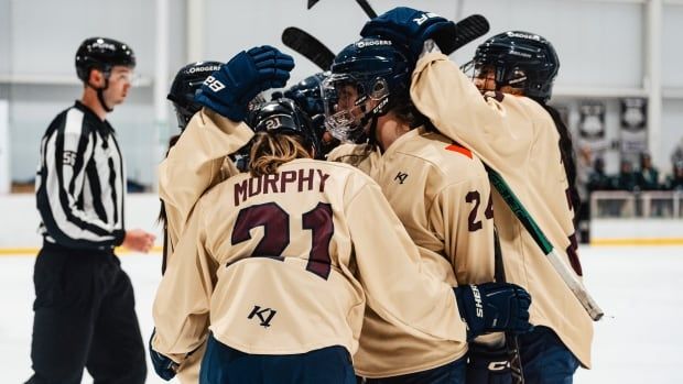 Several hockey players wearing cream-coloured jerseys celebrate on the ice.