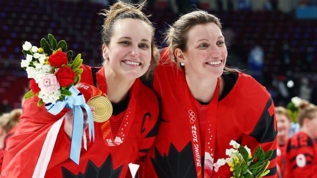 Two women's hockey players pose for a photograph, while one holds a gold medal.