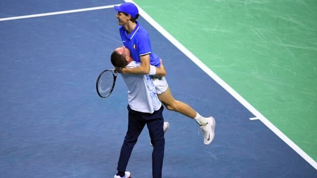 A men's tennis player is lifted in the air by a coach while on the court.