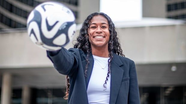 A woman poses with a soccer ball.