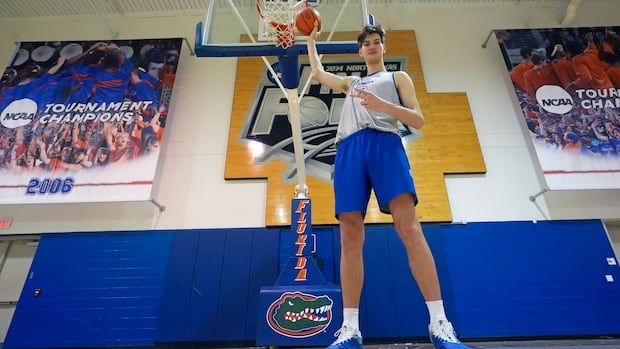 Tall man with blue shoes, holding a basketball underneath a basketball rim. 