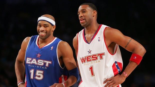 Two basketball players laugh together on the court during the 2005 NBA All-Star Game.