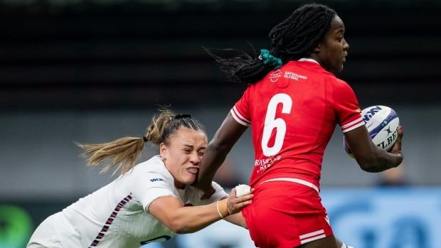 A female rugby player is seen with the ball as she's pressured by an opposition player.