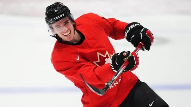 A hockey player wearing a red jersey smiles after shooting the puck.