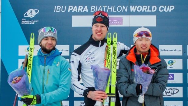 Three male Para biathletes stand on a podium.