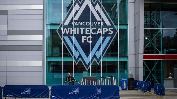 Next to a glass entryway, a one-storey tall glass sign with the Whitecaps logo reads, Vancouver Whitecaps FC.