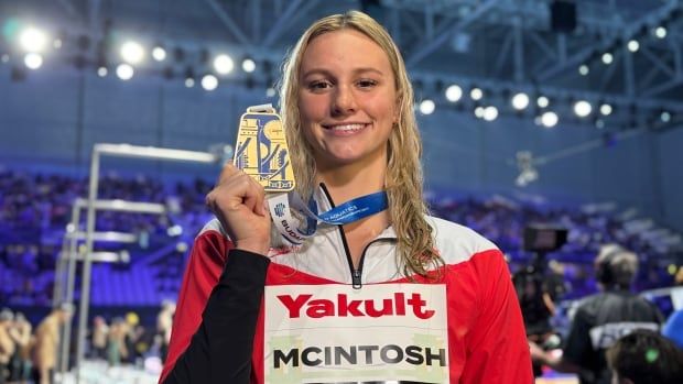 A woman holds up a gold medal.