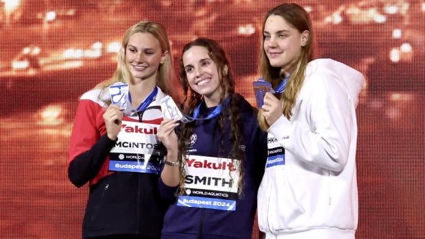 Three women's swimmers pose for a photograph while holding the medals draped around their necks.