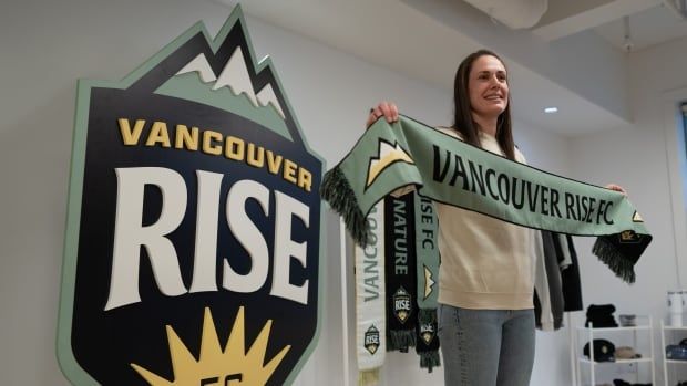 A woman holds up a scarf that reads Vancouver Rise FC.