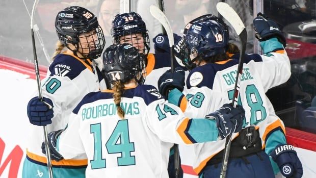 A group of women's hockey players huddle together on the ice while celebrating a goal.