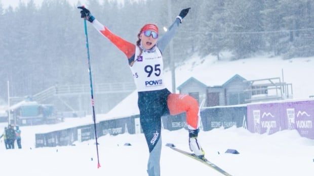 A female Para cross-country skier raises her arms while shouting in celebration on a race course.