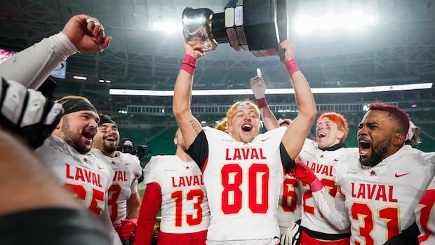 Man in white and red football jersey holds football trophy with teammates in the background wearing the same jersey colour scheme