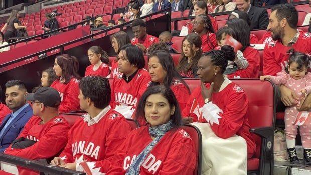 People wearing red Canadian hockey jerseys and holding miniature Canadian flags seated in a hockey arena