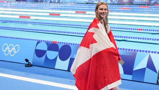 A swimmer smiles while draped in a Canadian flag.