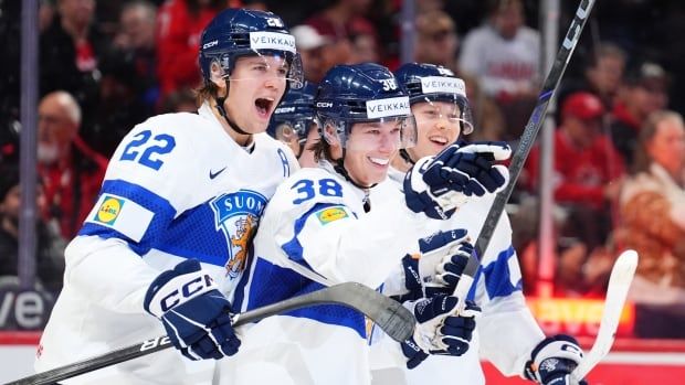 Male ice hockey players smile while celebrating on the ice inside an arena filled with fans.