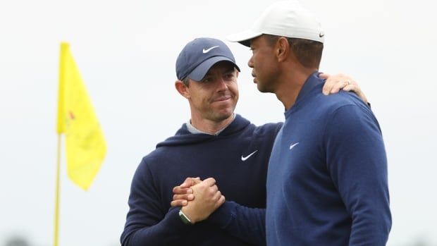 Two male golfers shake hands on a course during the day.