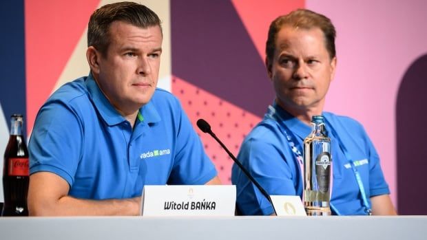 Two men sit in front of a microphone at a table during a press conference.