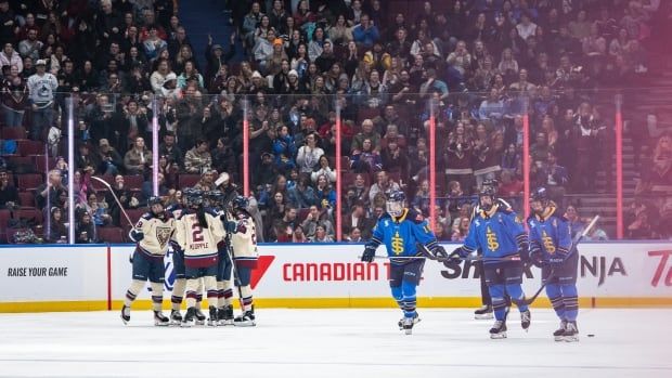 A large crowd cheers as some hockey players celebrate, while others walk away dejectedly.