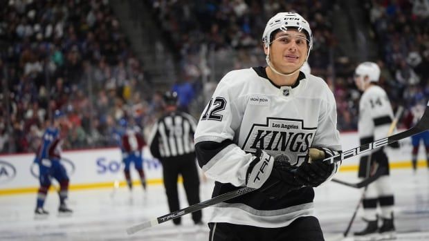 A hockey player in a white Kings jersey looks upwards as he skates between whistles during an NHL game.