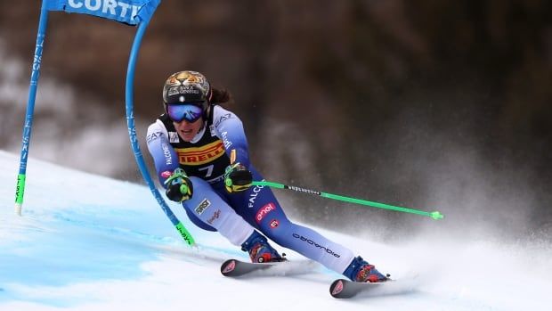 A female alpine skier leans to her right while racing past an obstacle during a super g event.