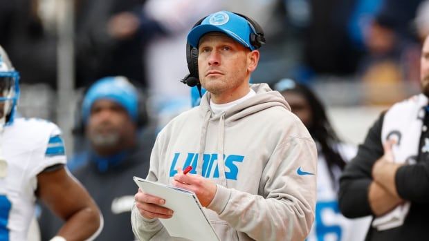 A men's football coach looks on from the sidelines during a game.