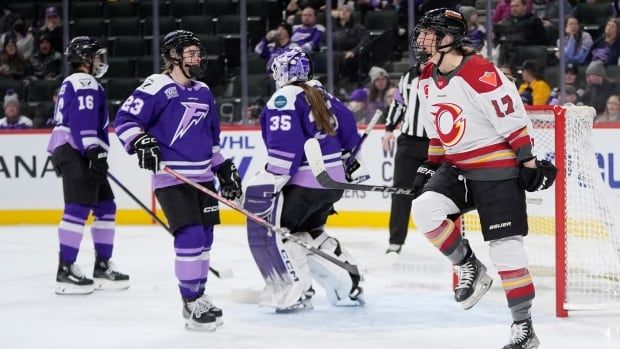 A group of women's hockey players in purple jerseys are shown at centre, while a player in a white, red, and yellow jersey celebrates, at left.