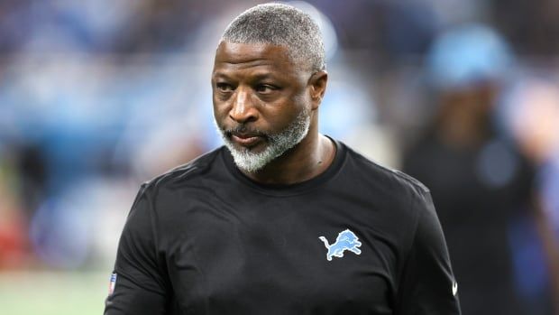 A male football coach watches during warmups before an NFL game.