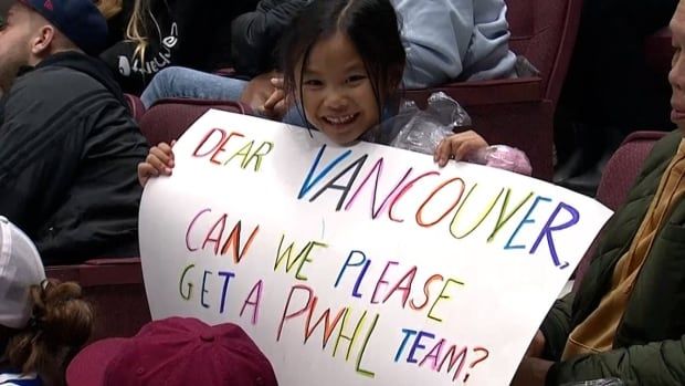 A young PWHL fan holds a homemade sign that reads 'DEAR VANCOUVER, CAN WE PLEASE GET A PWHL TEAM?'