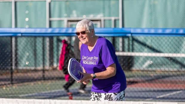 A woman in a purple shirt plays pickleball.