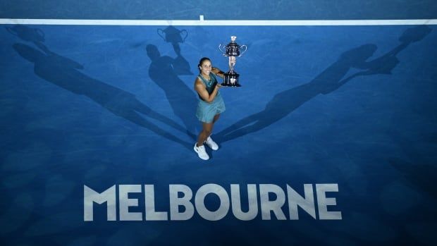 A women's tennis player holds a trophy with the word 'MELBOURNE' spelled out on the court.