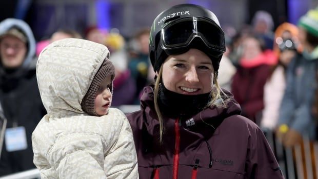 A female skier smiles while holding her daughter after an event.