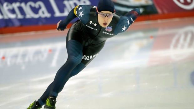 A male speed skater skates around a corner during a race.