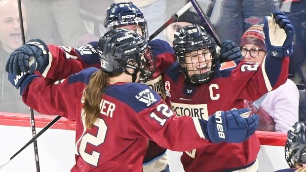 Three women's hockey players celebrate near the boards.