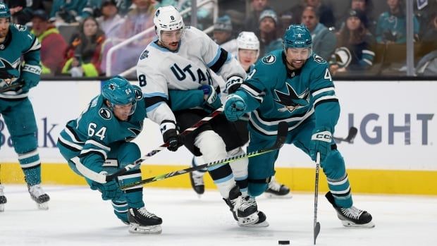 Three male hockey players fight for puck.