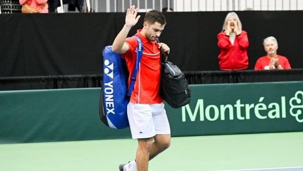 Male tennis player waves with his right hand as he walks off the court.