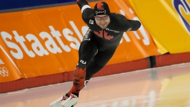 A male speed skater races around a corner with his right arm pointed behind him.