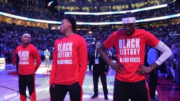 Men's basketball players stand during a singing of national anthems.