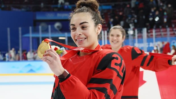 Women's hockey player holding olympic gold medal for the camera