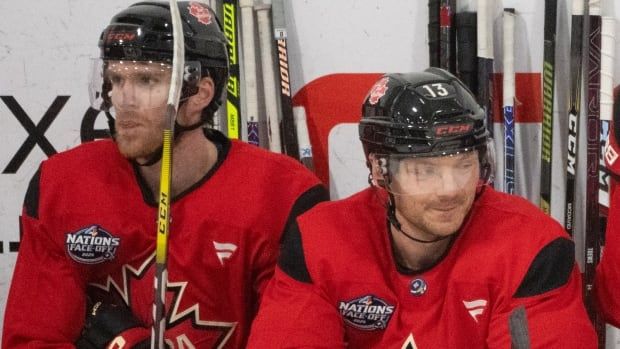 Tso hockey players in red jerseys sit next to each other on a bench.