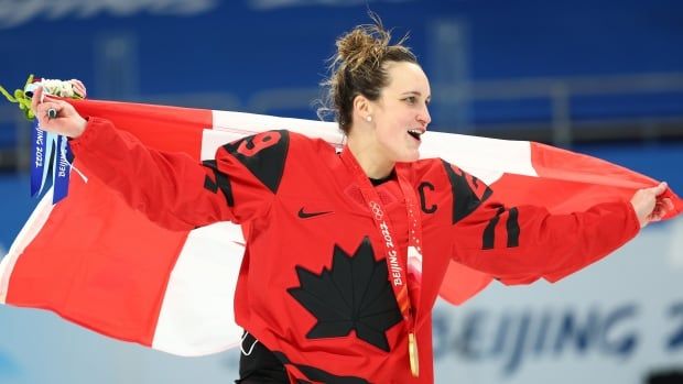 A women's hockey player celebrates with a Canadian flag.