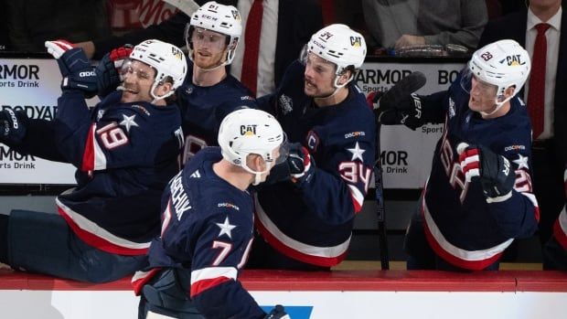 A men's hockey player skates by his team's bench where his teammates reach out for high-fives.