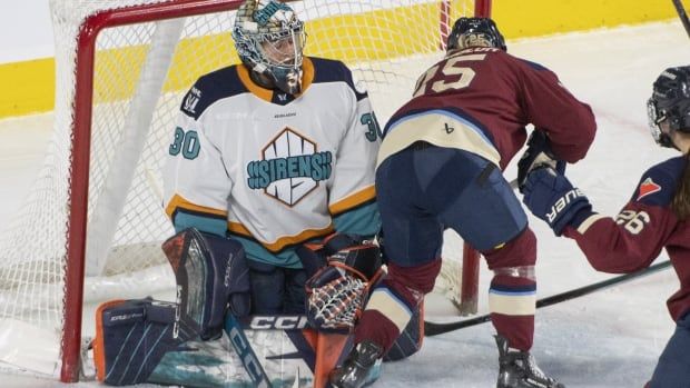 A female ice hockey player scores from close range against a goaltender down on her knees.