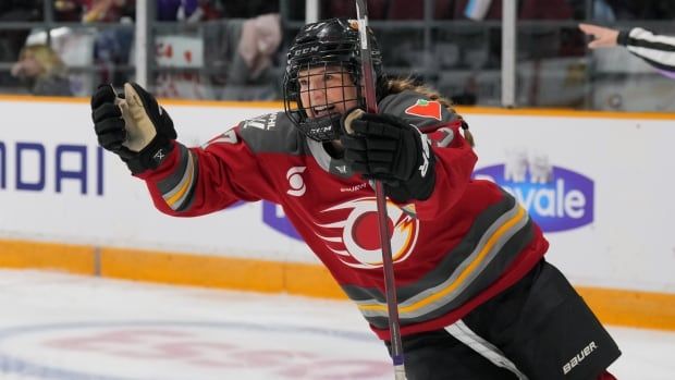 A female ice hockey player smiles while raising her arms in celebration during a game.