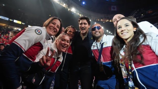 A group of athletes pose for a photo with Prime Minsiter Justin Trudeau in an arena.