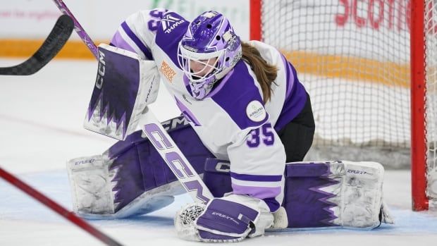 A goaltender kneels on the ice and covers the puck with her glove.