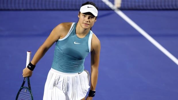 A women's tennis player is shown holding her racquet as she faces away from the net.